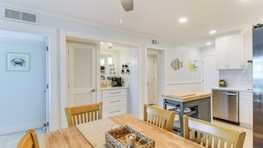 A modern kitchen with white cabinetry, a stainless steel dishwasher, and a wooden dining table with chairs. - Beachfront Retreat w/ Pool Access in Gulf Shores! (Gulf Shores)