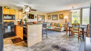A spacious kitchen with wooden cabinets, a black microwave, and a large island. There is a dining area with a table and chairs, and a sofa in the background. - 2 Mi to Town: Oceanside Kailua-kona Paradise! (Kailua-Kona)