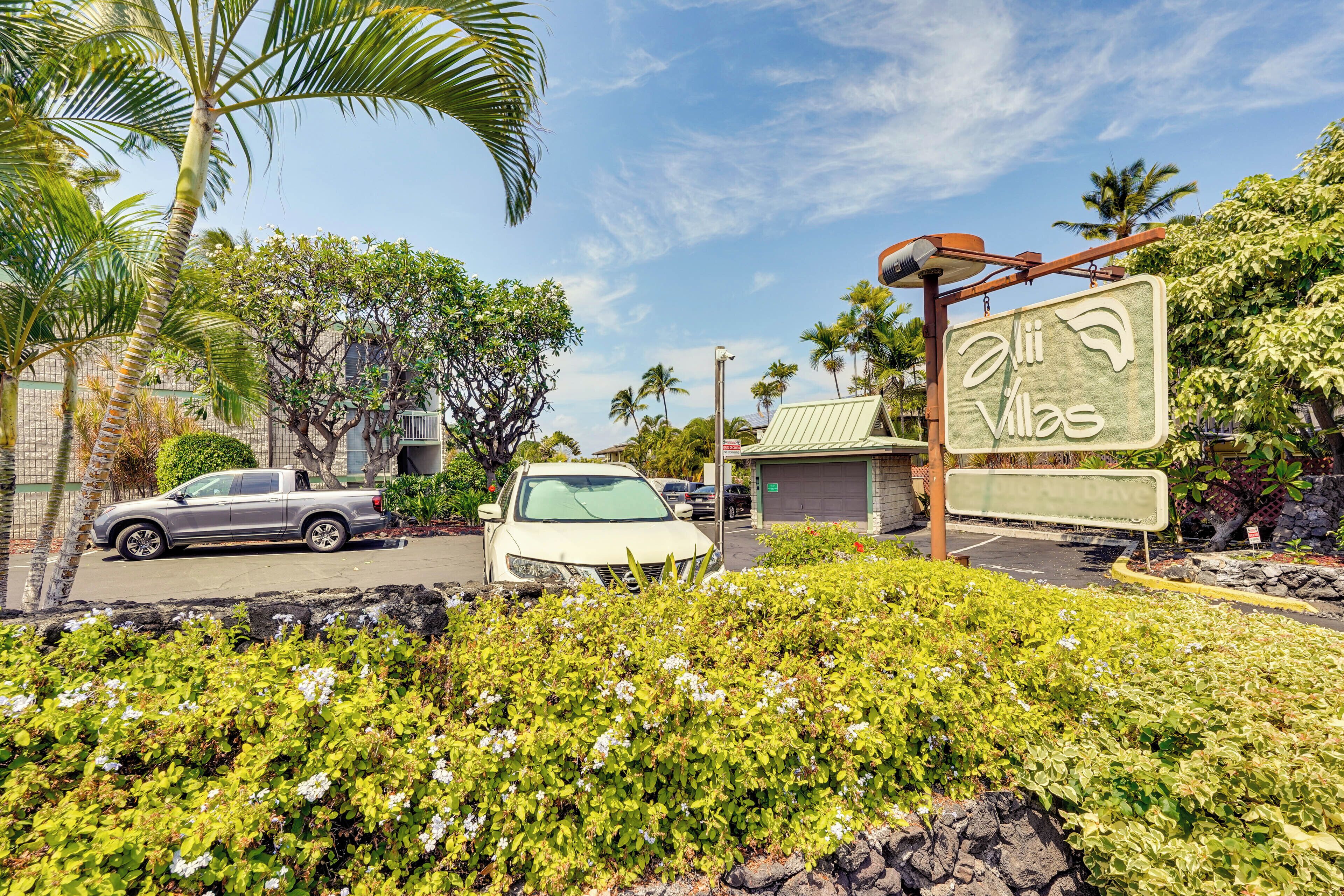 A sign for 'Aii Villas' with a parking area and vehicles in the foreground.