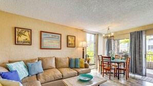 A living room with a beige sofa, a coffee table, and a dining area with wooden chairs and a table. - 2 Mi to Town: Oceanside Kailua-kona Paradise! (Kailua-Kona)