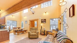 A spacious living area with a wooden ceiling, a large window, a cozy fireplace, and a dining table with chairs. - 5 Mi to Kasilof River: Forest-view Retreat w/ Deck (Kasilof)