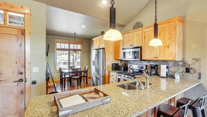 A kitchen with granite countertops, wooden cabinets, stainless steel appliances, and bar stools. - Mountain-view Cabin Near Trails in Powell Butte! (Powell Butte)