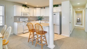 A modern kitchen with white cabinetry, a central island, and two wooden chairs. - Walk to Beach: Wildwood Apt w/ Balcony! (Wildwood)
