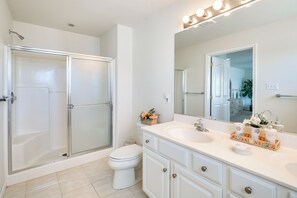 Ein modernes Badezimmer mit einer gläsernen Duschkabine, einer weißen Toilette und einem Waschtisch mit zwei Becken und einem großen Spiegel.