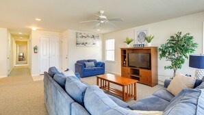 A living room with a large blue sofa, a wooden coffee table, a television on a wooden stand, and a ceiling fan. - Walk to Beach: Wildwood Apt w/ Balcony! (Wildwood)