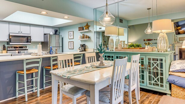 A modern kitchen with a central island, white bar stools, and a dining table with chairs. - 7 Mi to The Wharf: Gem w/ Beach Access (Orange Beach)