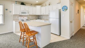 A kitchen with white cabinets, a central island with two wooden stools, a refrigerator, and a microwave. - Half-mi to Wildwood Boardwalk: Family-friendly Apt (Wildwood)