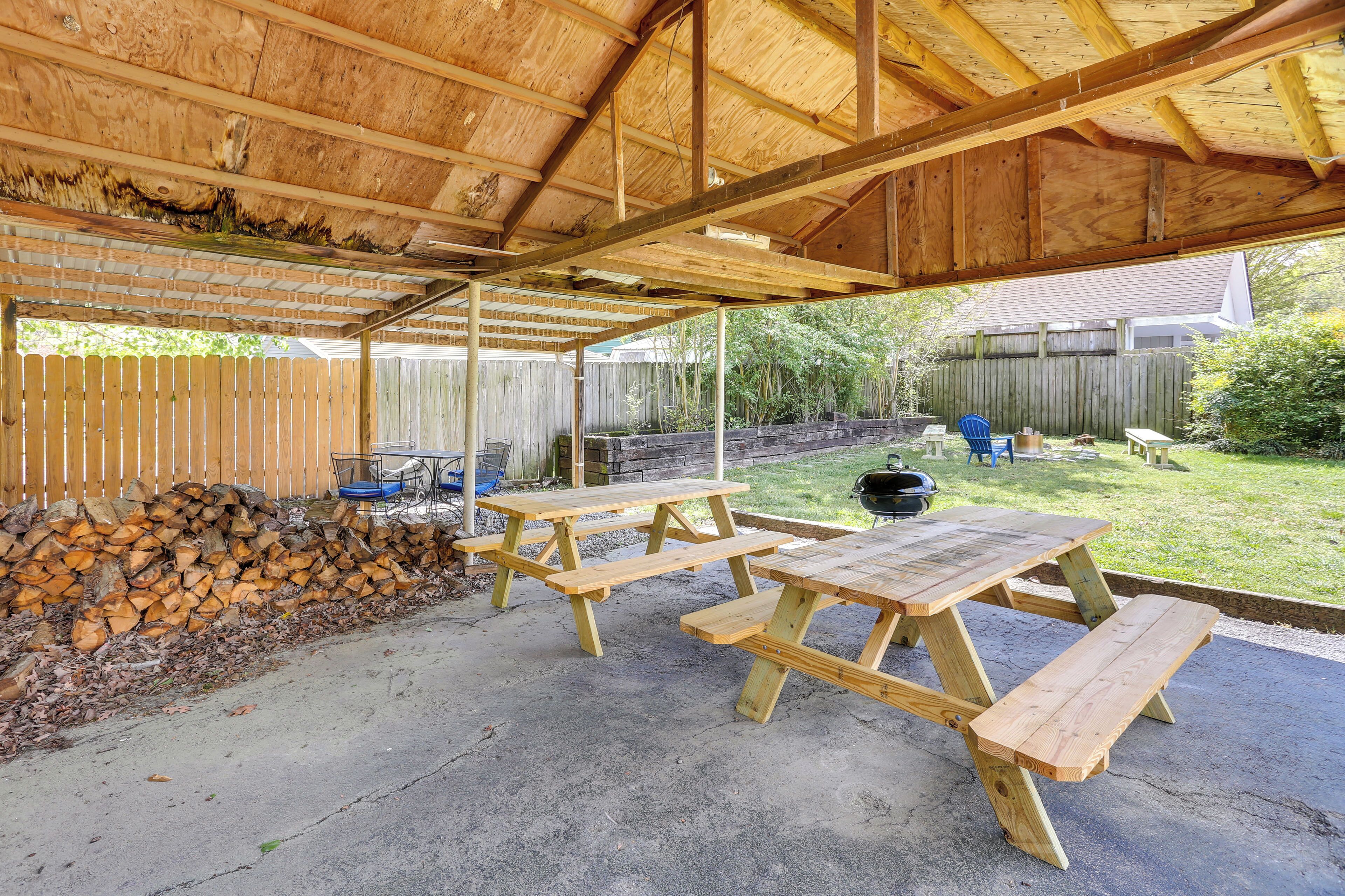 A covered patio with wooden picnic tables and a stack of firewood.