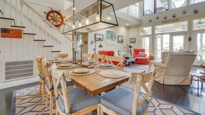 A spacious dining area with a wooden table set for six, surrounded by wooden chairs with grey cushions. A large wooden ship's wheel decorates the wall above the staircase. - Marina & Golf Course Views: Edisto Island Home (Edisto Island)