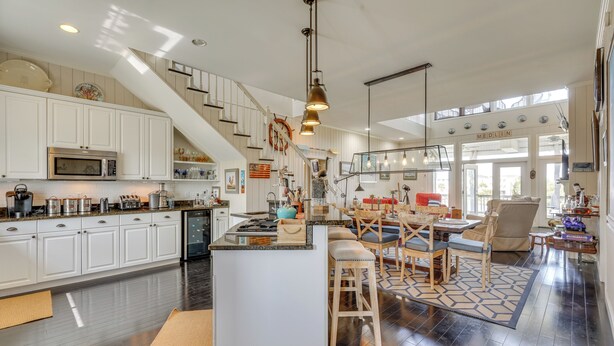 A spacious kitchen with white cabinets, a central island, and a dining area with wooden chairs and a patterned rug. - Marina & Golf Course Views: Edisto Island Home (Edisto Island)