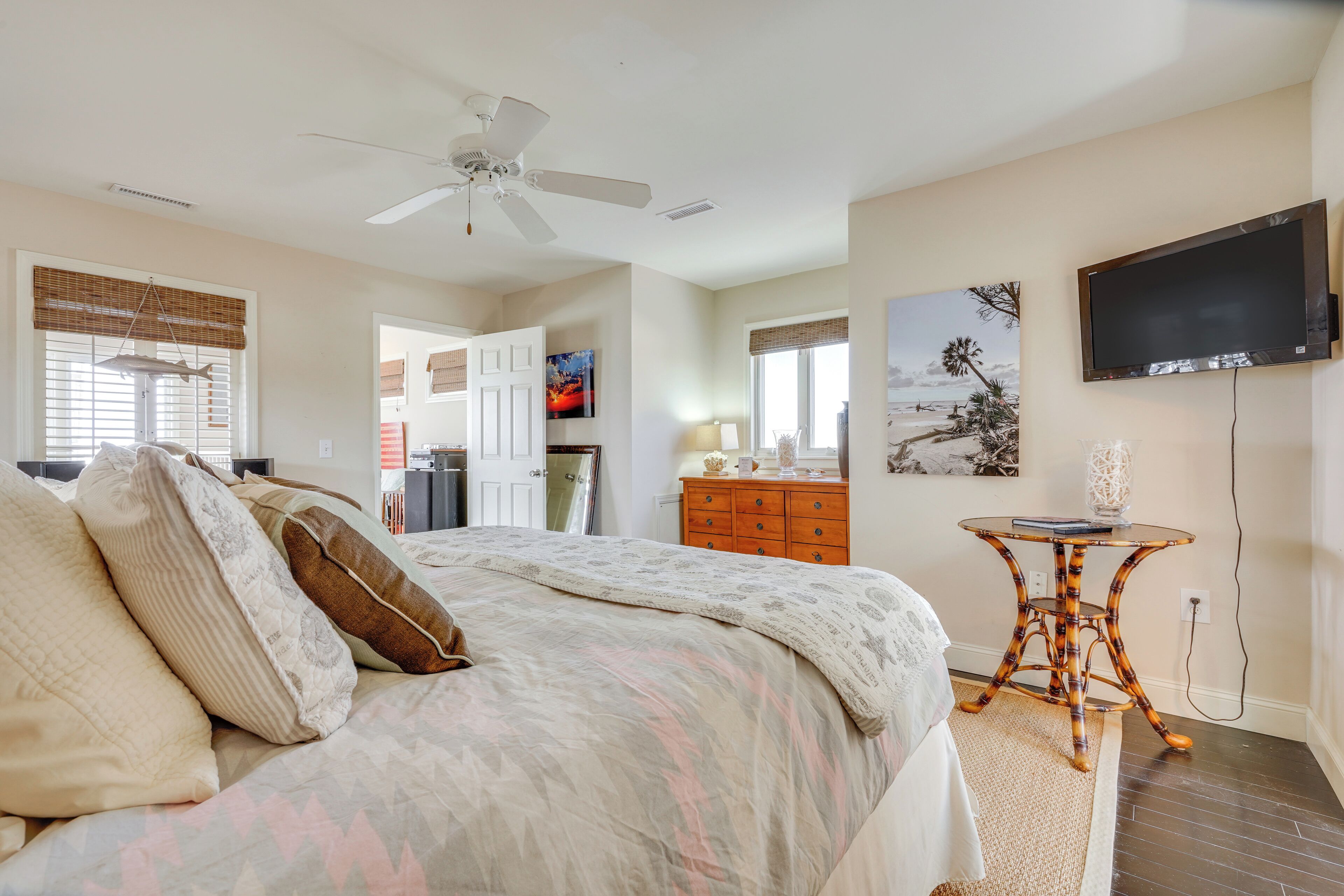 A bedroom with a bed, a ceiling fan, a TV, and artwork on the wall.