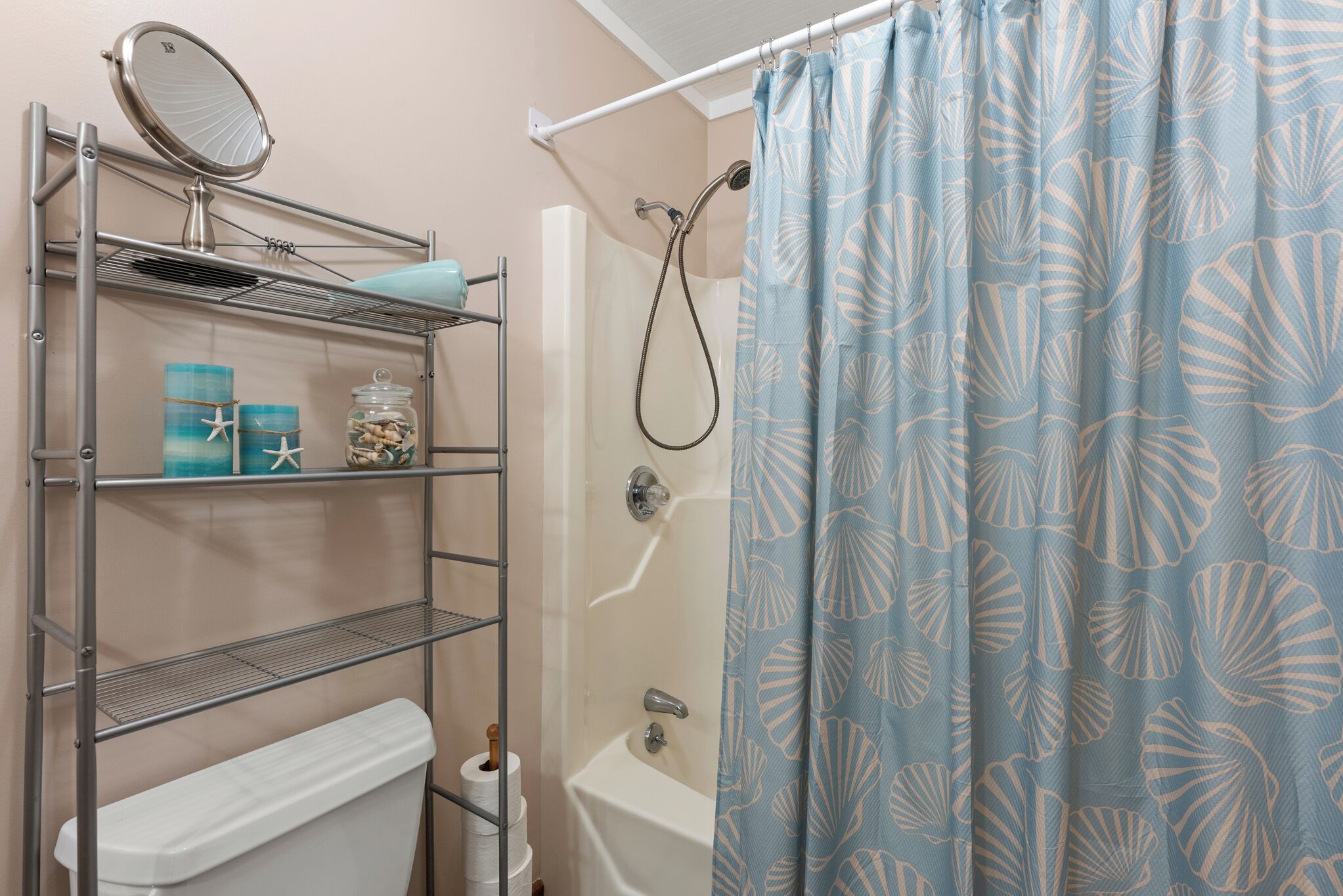 A bathroom with a shower, a toilet, a shelf with toiletries, and a curtain with a shell pattern.