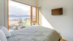 Un dormitorio con un ventanal grande, una cama y un televisor de pantalla plana montado en la pared.