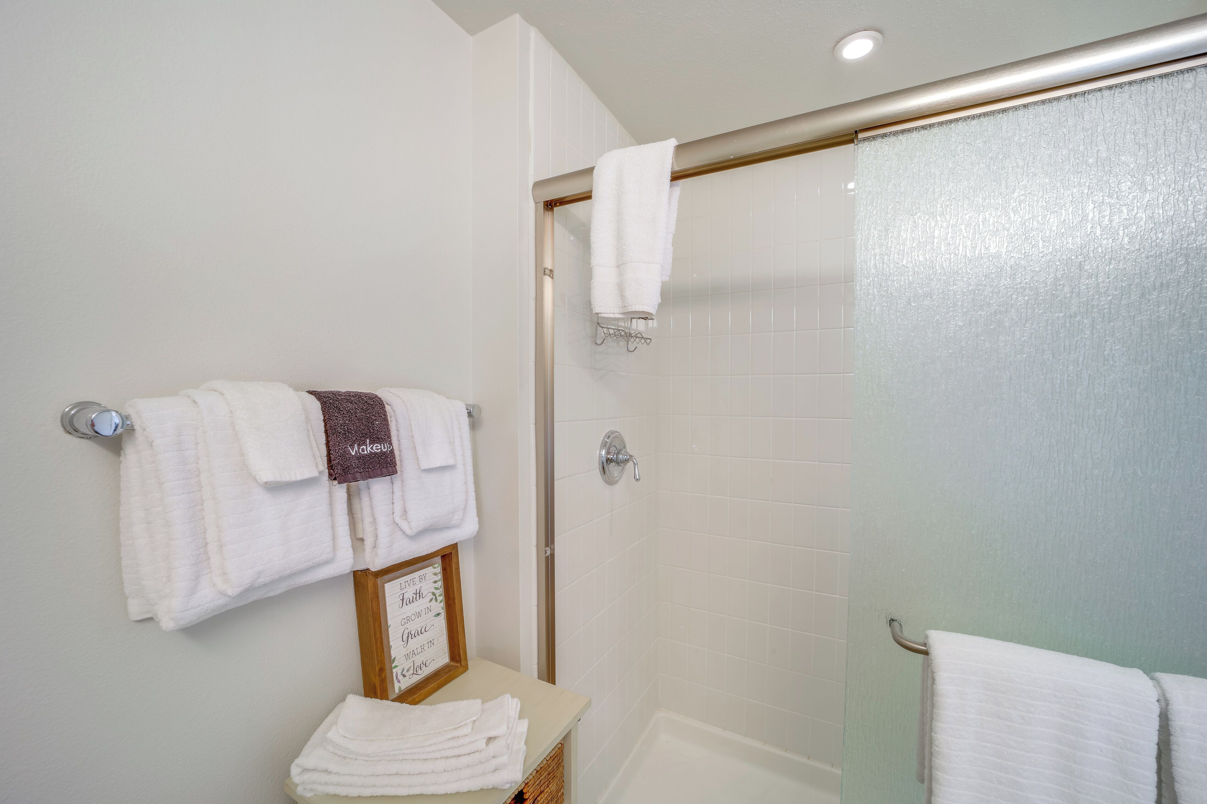 A bathroom with a glass shower door, white towels, and a framed inspirational quote on the counter.