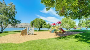 Un parque infantil con estructuras para escalar y toboganes, rodeado de árboles y un lago.