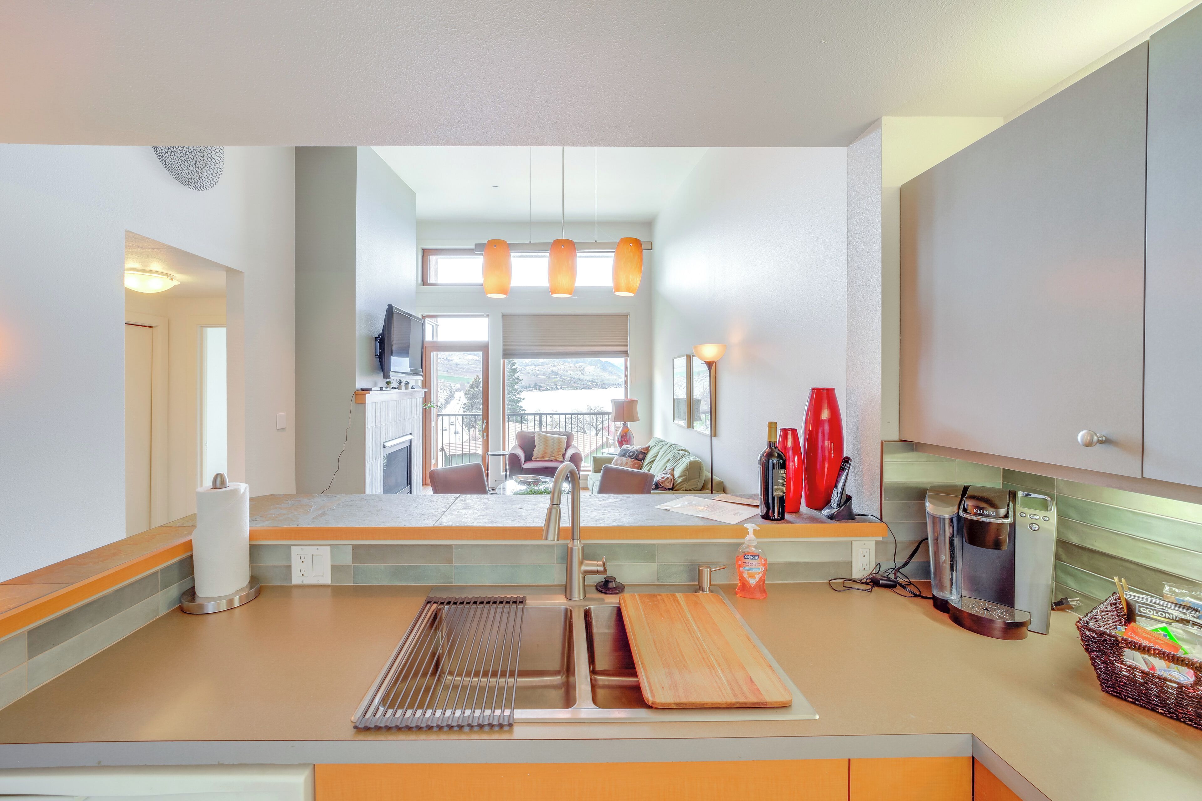 A modern kitchen with a built-in oven, a coffee maker, and a sink. There is a window overlooking a balcony with outdoor furniture.