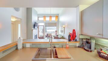 A modern kitchen with a built-in oven, a coffee maker, and a sink. There is a window overlooking a balcony with outdoor furniture.