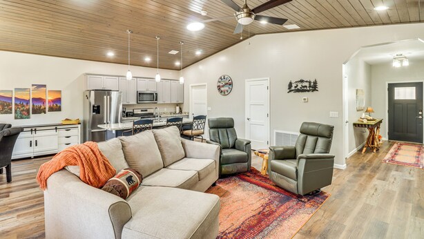 A spacious living room with a beige sofa, two leather chairs, a wooden ceiling, and a kitchen in the background. - Hot Tub & Outdoor Living: Relaxing Show Low Cabin (Show Low)