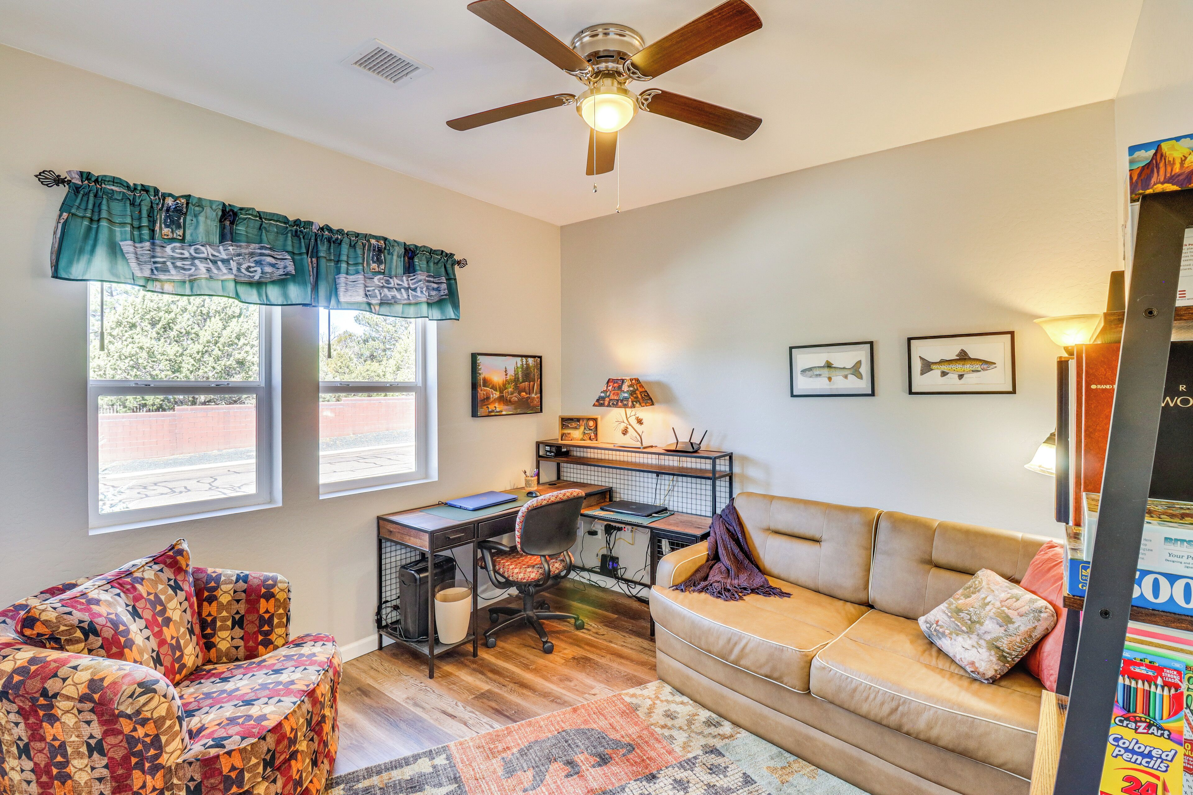 A room with a desk, a couch, a ceiling fan, and a window with curtains.