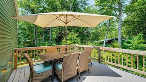 Eine Holzterrasse mit Tisch und Stühlen, umgeben von einem Hollerleger, vor einer Kulisse aus üppigem Grün.