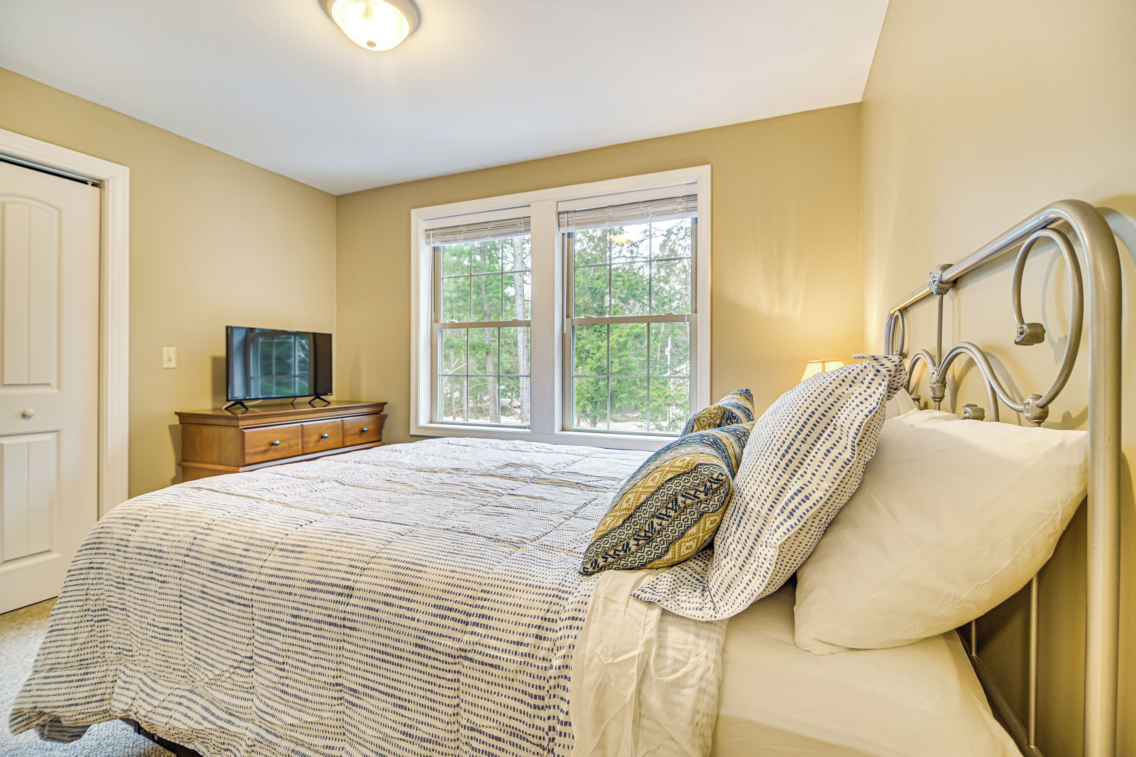 A bedroom with a bed, a dresser, a television, and a window.