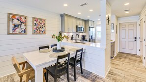Een moderne keuken met witte kasten, een centraal eiland en een eethoek met een witte tafel en donkere stoelen.