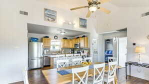 A spacious kitchen with wooden cabinets, a stainless steel refrigerator, and a dining area with a wooden table and white chairs. - 1 Block to Surfside Beach: Home w/ Gulf Views! (Freeport)