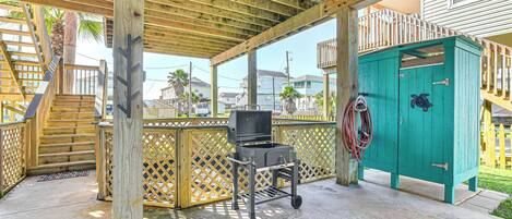 A covered outdoor area with a wooden deck, a grill, and a green storage unit.