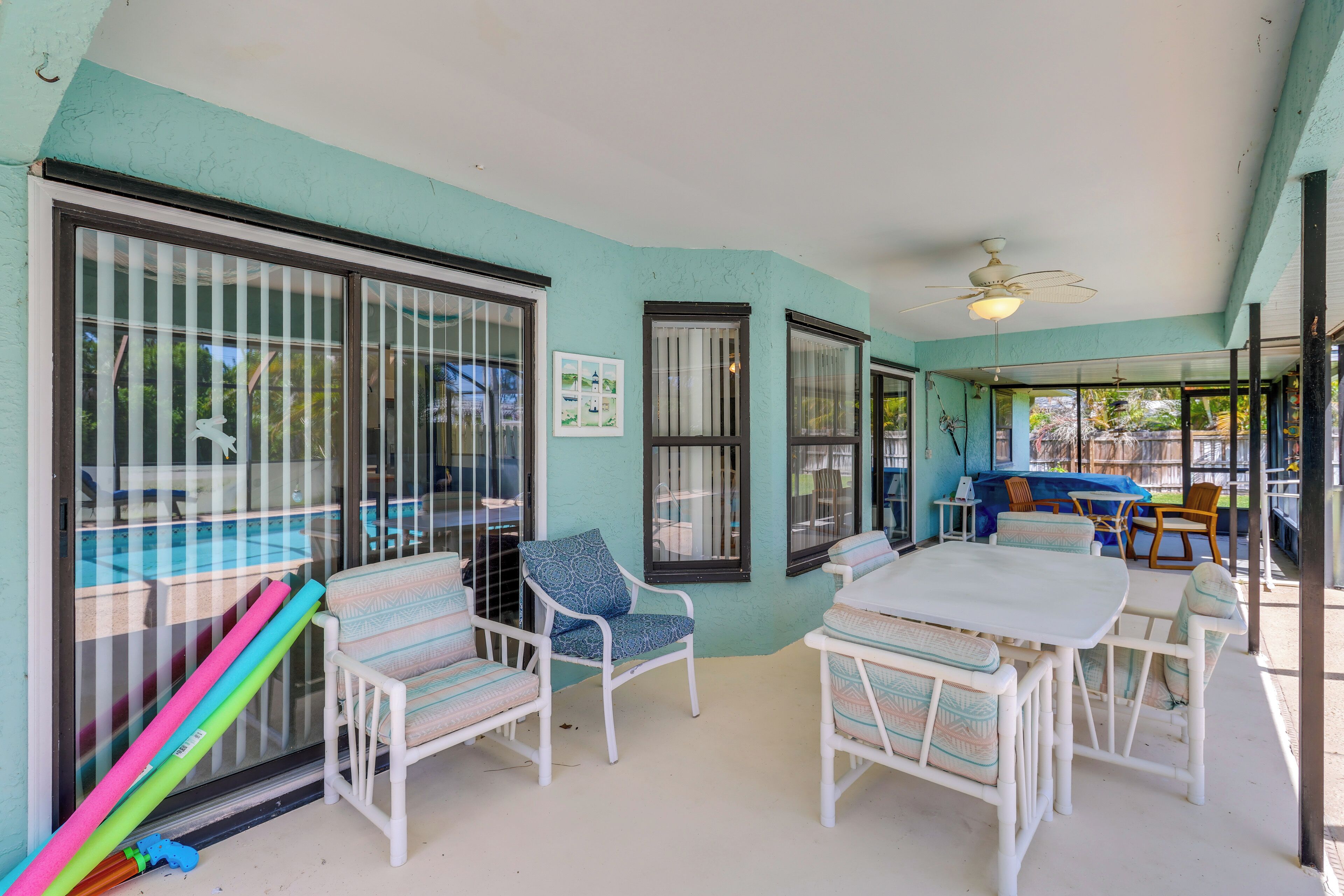 A covered patio area with a table and chairs, a ceiling fan, and a view of the pool.