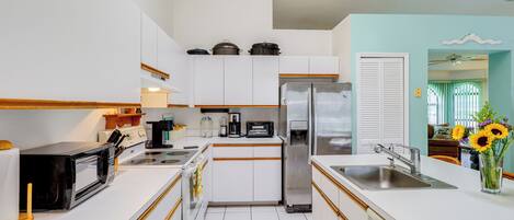 A modern kitchen with white cabinets, a stainless steel refrigerator, a microwave, and a sink.
