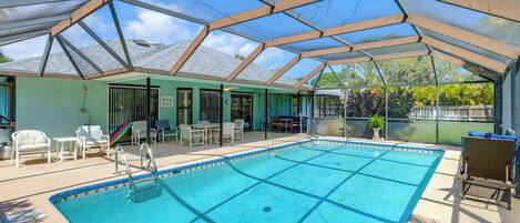 A covered swimming pool with a roof, surrounded by lounge chairs and a small table.