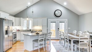 A modern kitchen with white cabinets, a stainless steel refrigerator, and a wooden dining table with chairs. - Modern Retreat w/ Mtn Views in Maggie Valley! (Maggie Valley)
