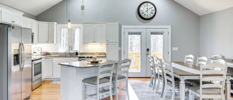 A modern kitchen with white cabinets, a stainless steel refrigerator, and a wooden dining table with chairs.