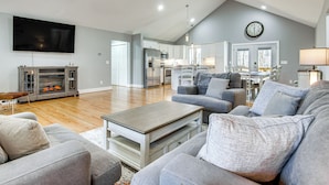 A spacious living room with a flat-screen TV, a fireplace, and a kitchen in the background. - Modern Retreat w/ Mtn Views in Maggie Valley! (Maggie Valley)
