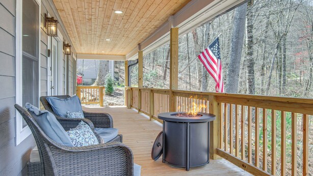 A covered deck with wicker chairs, a fire pit, and an American flag. - Modern Retreat w/ Mtn Views in Maggie Valley! (Maggie Valley)