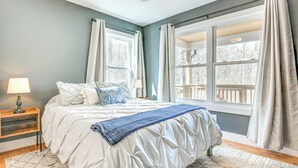 A bedroom with a bed, two windows, a nightstand, and a lamp. - Modern Retreat w/ Mtn Views in Maggie Valley! (Maggie Valley)