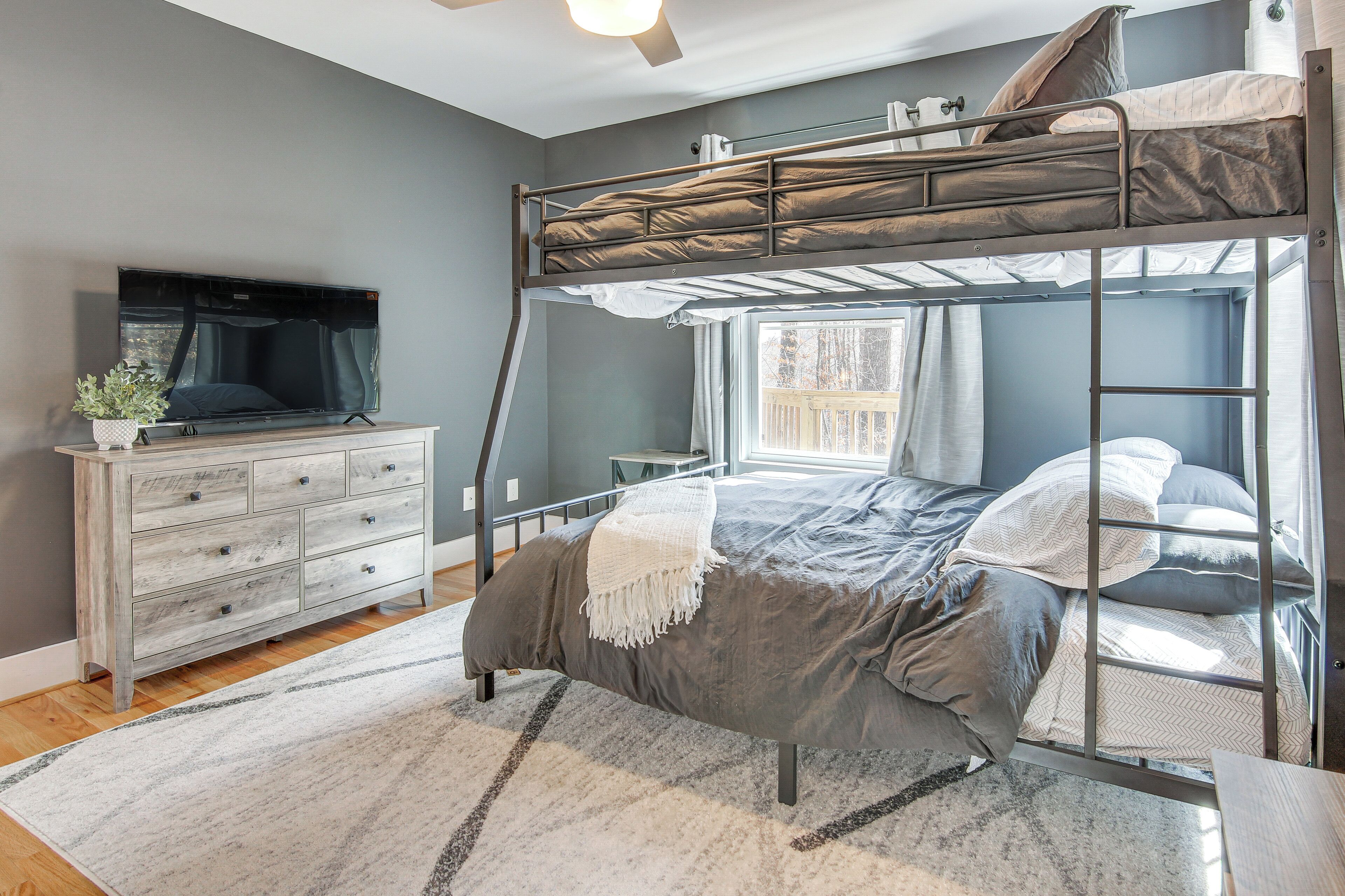 Une chambre avec un lit superposé, une télévision, une commode et une fenêtre avec des rideaux.