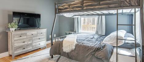 A bunk bed room with a TV, dresser, and a window with curtains.