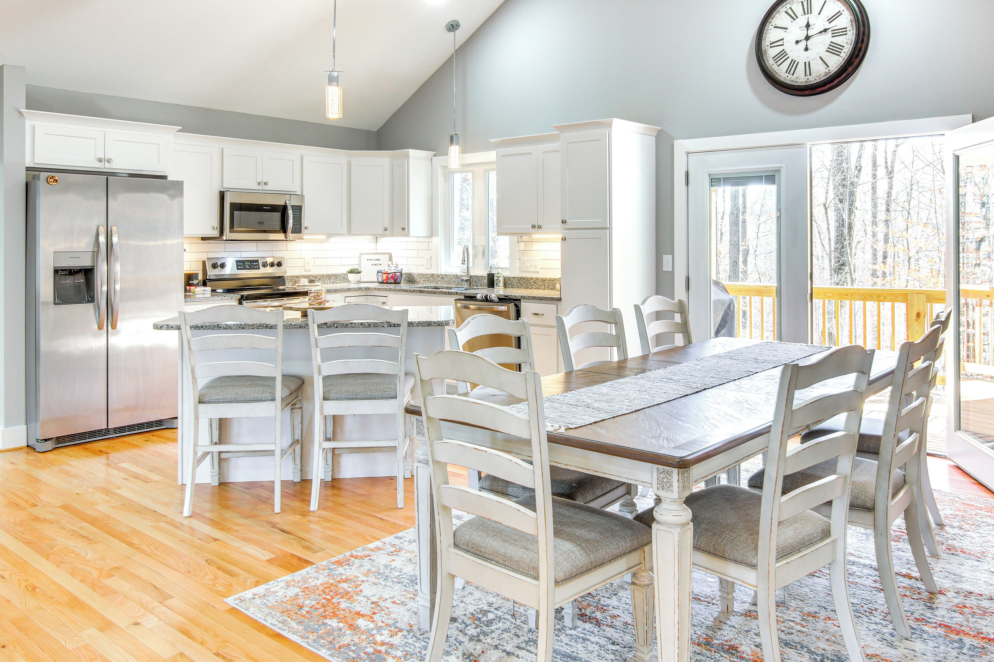 A modern kitchen with white cabinets, stainless steel appliances, and a dining area with a wooden table and white chairs.