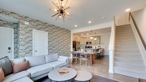 A modern living room with a gray sectional sofa, two round coffee tables, and a brick accent wall. - Modern Downtown Apt w/ Balcony in Wake Forest! (Wake Forest)