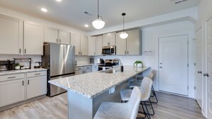 A modern kitchen with white cabinets, stainless steel appliances, and a granite countertop. There are bar stools and a white door in the background. - Modern Downtown Apt w/ Balcony in Wake Forest! (Wake Forest)