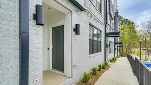 A modern building with a white brick facade, a covered entrance, and a pathway leading to a pool. - Modern Downtown Apt w/ Balcony in Wake Forest! (Wake Forest)