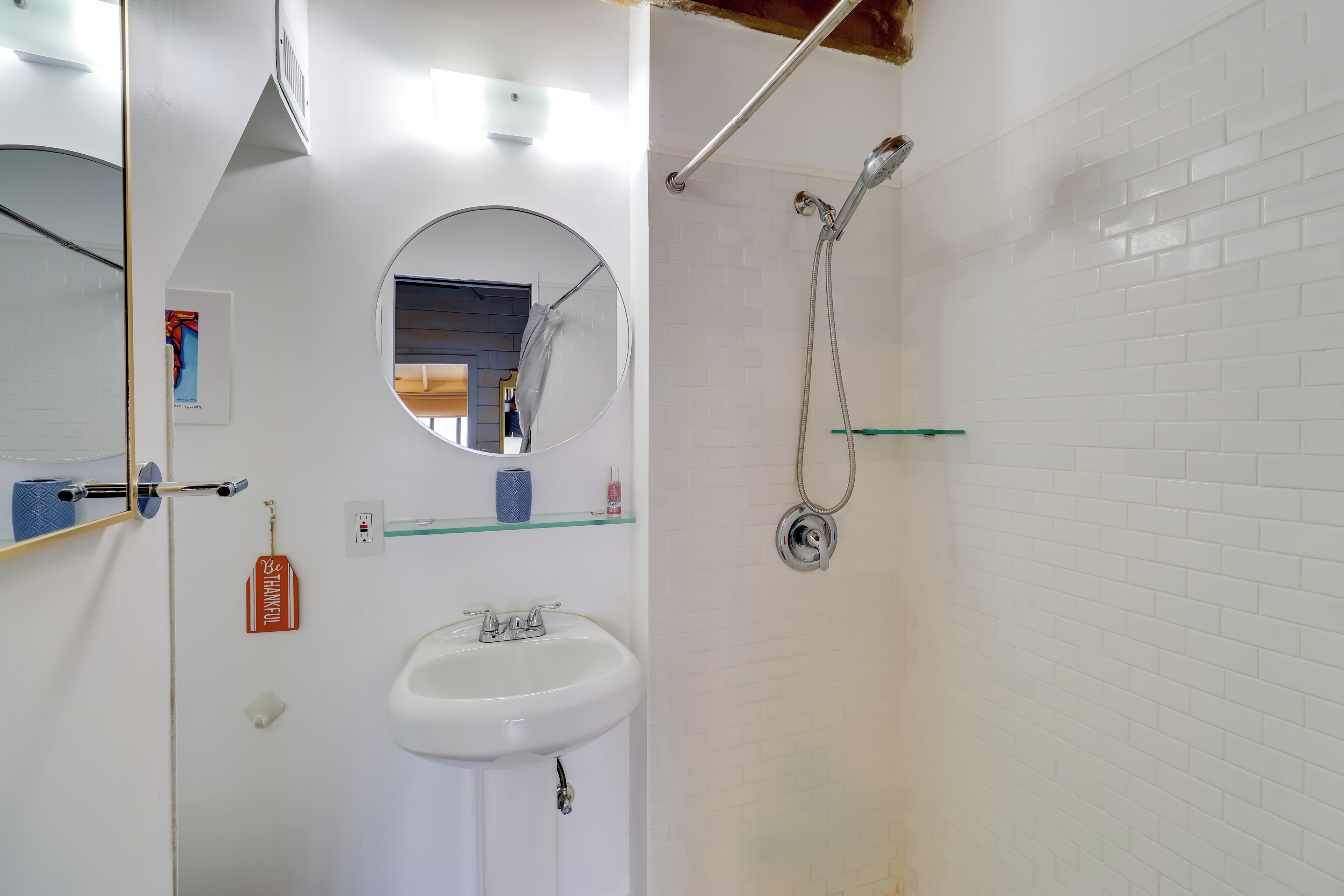 Un baño con lavamanos blanco, espejo, ducha y barra para toallas.