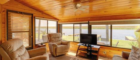 A cozy room with a wooden ceiling, large windows, a TV, and comfortable seating.