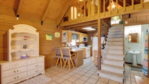 Un interior de madera con una zona de cocina, una mesa de comedor y una escalera que lleva a un nivel superior.