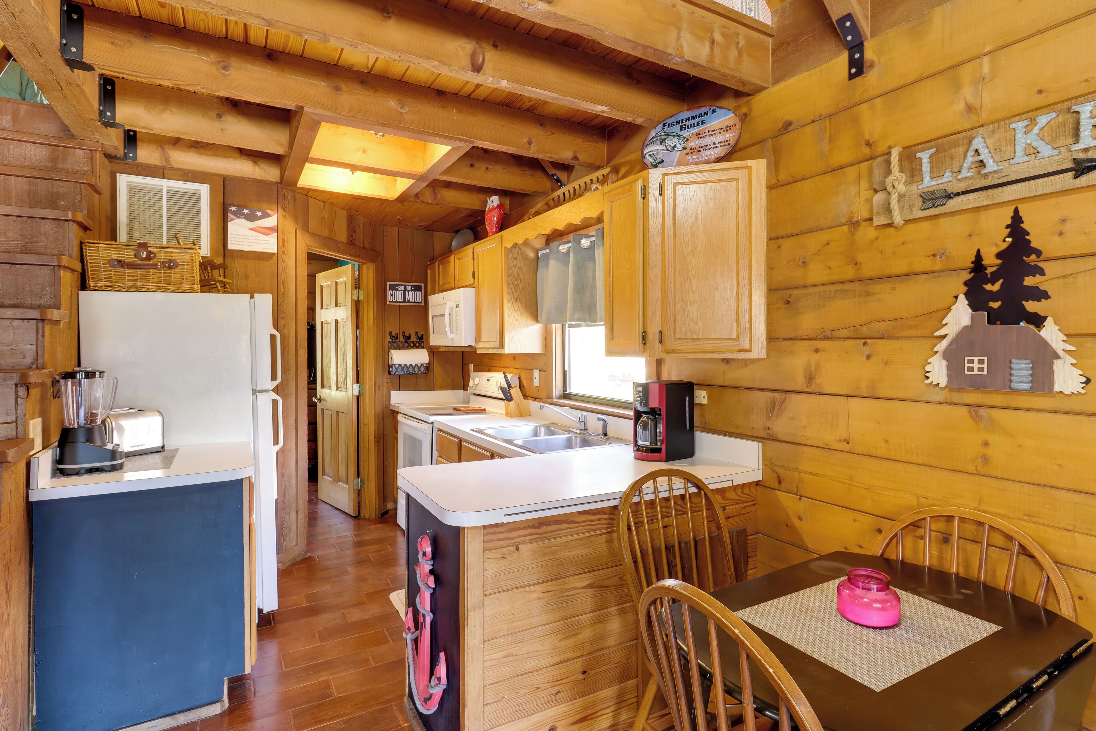 Interno di una baita in legno con cucina, zona pranzo e un cartello con scritto 'LAKE'.