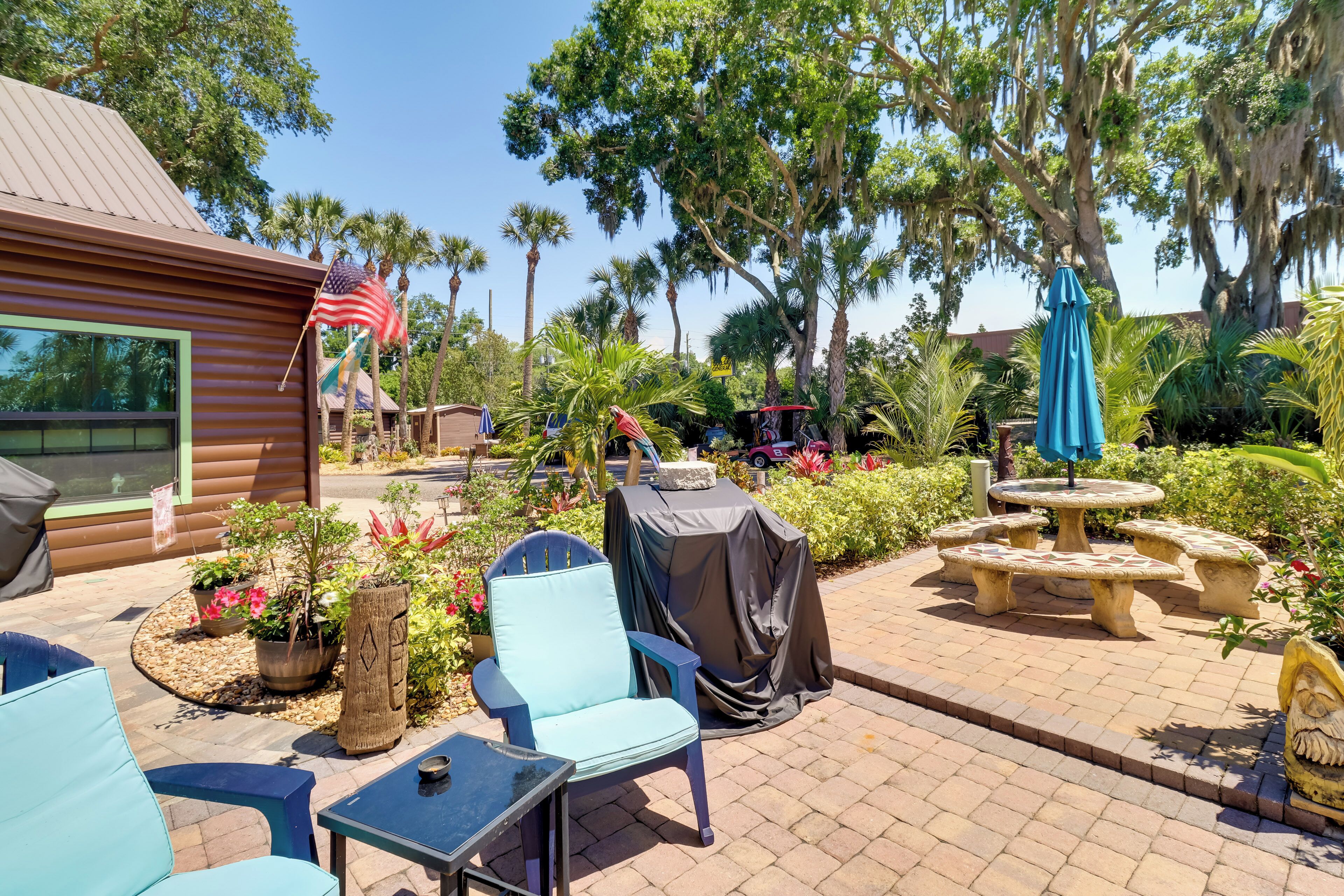Un patio exterior con zona de estar techada, una mesa con sombrilla azul y una pequeña fuente.