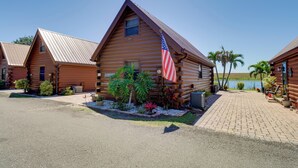 A wooden cabin with an American flag, surrounded by a gravel driveway and small plants. - Lake Okeechobee Cabin w/ Boat Launch & Patio (Okeechobee)