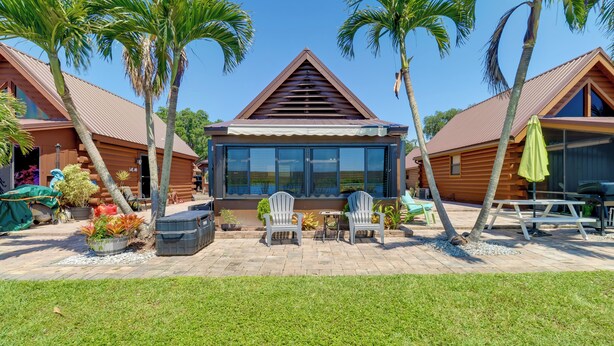 A wooden cabin with a large glass window, surrounded by palm trees and a patio with outdoor seating. - Lake Okeechobee Cabin w/ Boat Launch & Patio (Okeechobee)