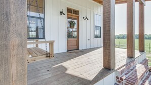 A wooden porch with a bench, a door, and a hanging flower basket. - Contrell Cottage On Farm w/ Peaceful Views (Lena)